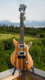 reclaimed from a ship's deck here in Kachemak Bay, doug fir body carved around the edges.  Solid surface bindings and whale's tooth with raven eye scrimshaw.  Maple neck  from left overs.
