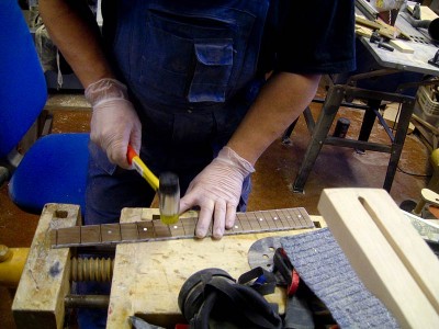 A plastic head hammer is a good tool to hammer in the frets, as it leaves no marks on the frets. Before I drive a fret into its slot I mask the fret slot edges with masking tape and flood the slot with CA glue.