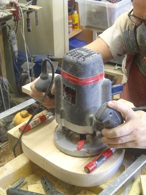 Routing a channel for the steel bar string retainer, using a 20 mm straight cut bit and a guide clamped to the body.